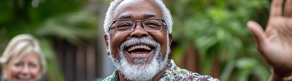 Senhor negro de cabelos e barba brancos dá um sorriso largo, enquanto acena