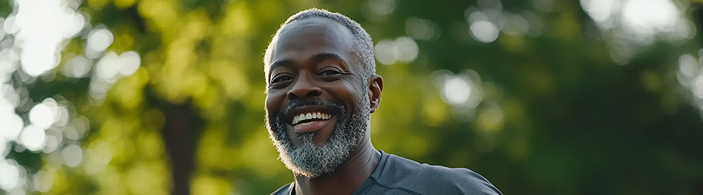 Senhor negro, de barba e cabelo já grisalhos, está correndo ao ar livre