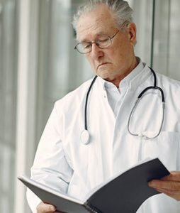Um médico idoso olha com atenção um prontuária de paciente