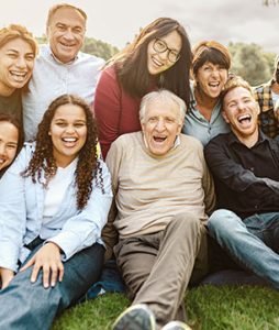 Um idoso está sentado no chão feliz da vida, com sua família ao seu redor.