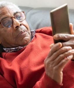 Senhor idoso está deitado no sofá e vê coisas pelo celular