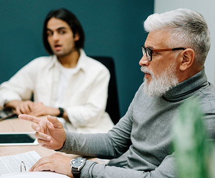 Um senhor idoso está em uma sala de reunião com um moço bem mais jovem