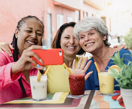 Três amigas sentadas tomando um suco, tiram uma self com o celular