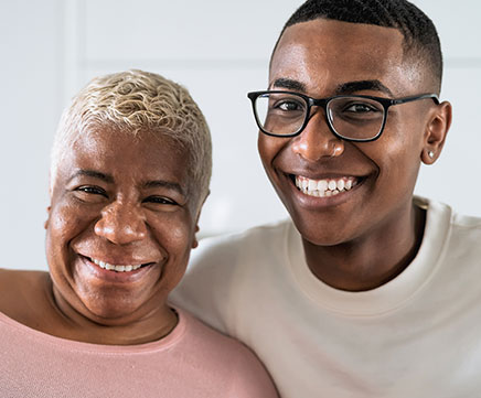 Uma senhora idosa recebe o abraço apertado de um jovem. Os dois sorriem animados