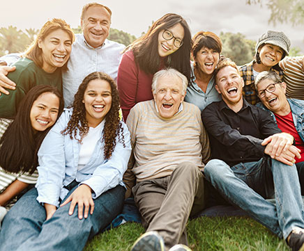 Um idoso está sentado no chão feliz da vida, com sua família ao seu redor.