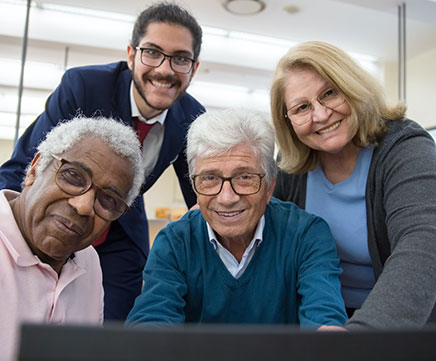 Três homens e uma mulher, estão olhando diretamente para uma tela de computador.