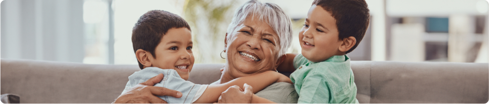 Senhora sorrindo, abraça seus dois netos