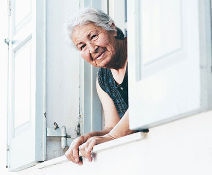 Senhora idosa espia pela janela de sua casa