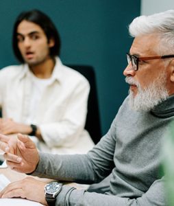 Um senhor idoso está em uma sala de reunião com um moço bem mais jovem