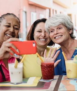 Três amigas sentadas tomando um suco, tiram uma self com o celular