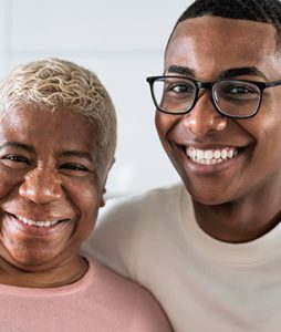 Uma senhora idosa recebe o abraço apertado de um jovem. Os dois sorriem animados