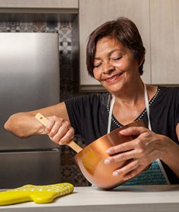 Uma senhora está em sua cozinha, mexendo com uma colher de pau em uma panela